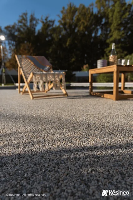 CREA devient Applicateur Agréé Résineo 2 Chaise longue et table en bois sur sol en gravier dans jardin ensoleillé