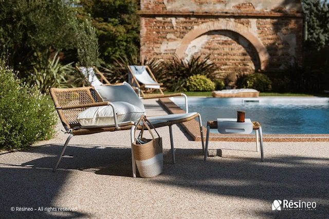 Chaise longue et tabouret près d'une piscine avec un mur en pierre en arrière-plan