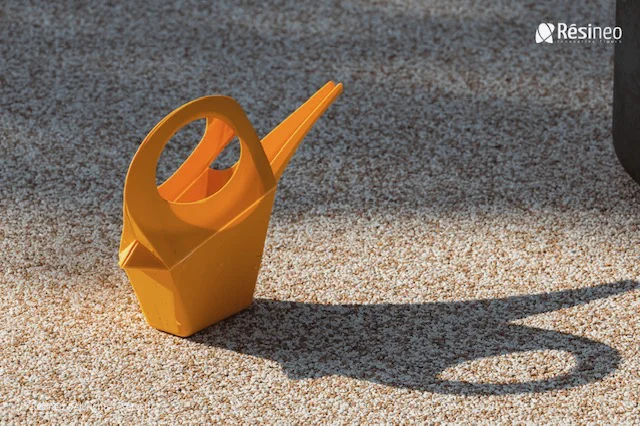 CREA devient Applicateur Agréé Résineo 7 Arrosoir en résine de couleur orange posé sur du gravier