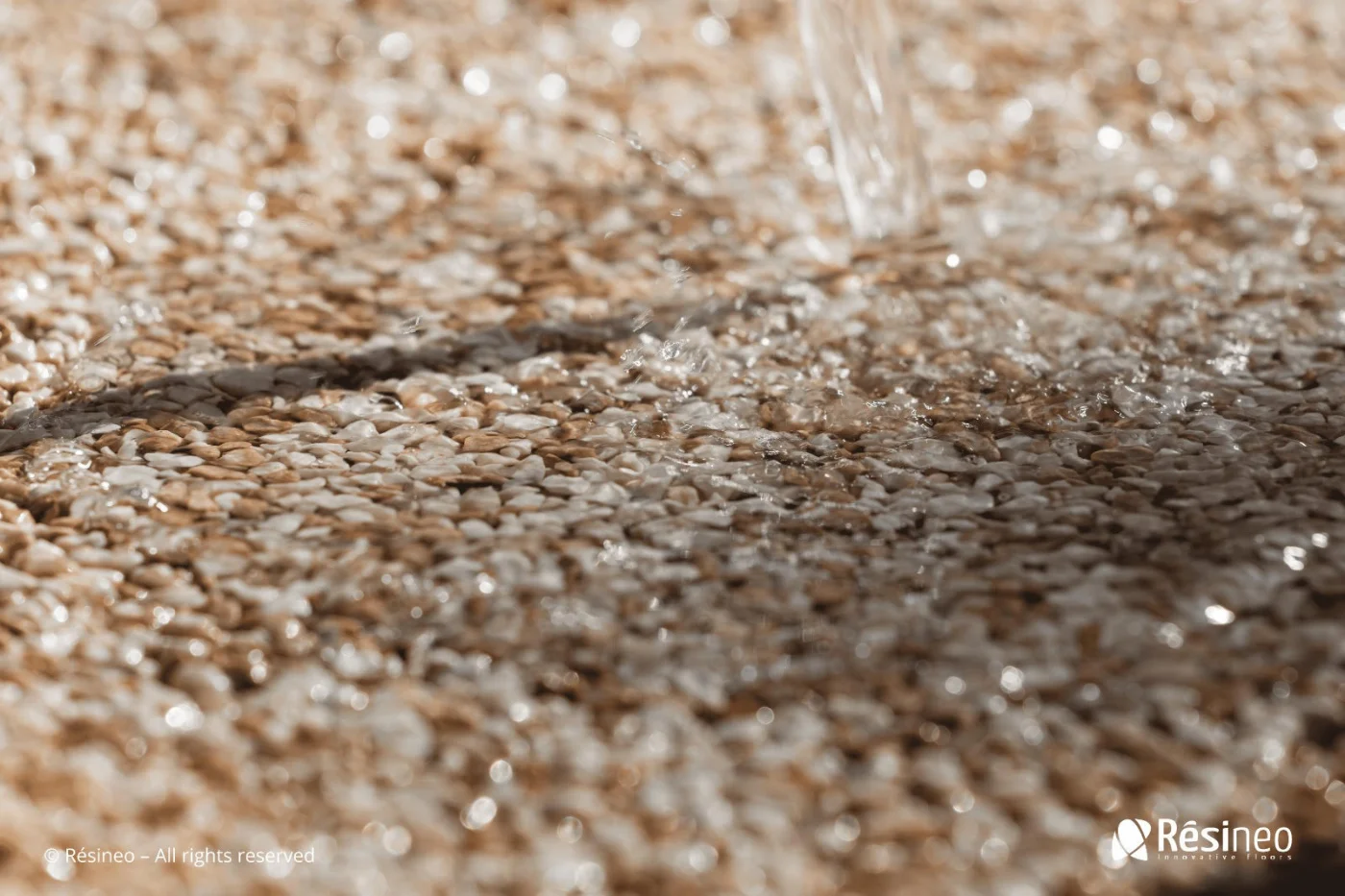 CREA devient Applicateur Agréé Résineo 5 Eau ruisselant sur des graviers ou galets, détail de texture naturelle.
